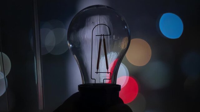 A broken light bulb in a hand against the backdrop of a nighttime city. Power outages due to the war in Ukraine.
