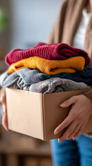 Person holding a cardboard box filled with neatly folded clothes symbolizing donation or relocation.
