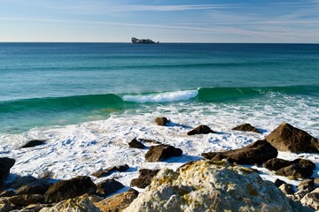 Rocky shoreline with turquoise wave and distant ship &mdash; calm seascape with copy space