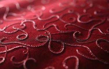 Close view of dark red fabric with intricate silver thread swirling patterns. This textile features delicate stitching details creating a rich textured surface, perfect for craft and design projects.