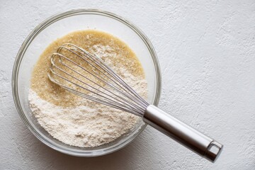 Whisk mixing flour and liquid batter in clear glass bowl
