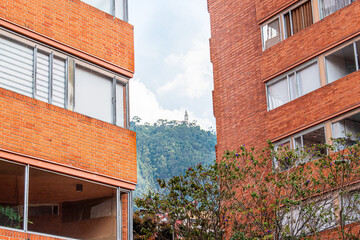 A calm urban scene shows red brick apartment blocks flanking a view of famous Bogota green hill topped by a distant structure.