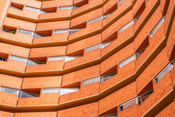 A striking red brick apartment building featuring angular, zigzag balconies that create a dynamic urban facade. Modern architecture and brick texture emphasize bold design and city living.