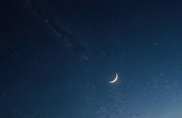 Crescent moon hangs in a vast starry night sky. Delicate clouds drift by on dark blue background. Celestial body glows with soft light. Beautiful cosmos.
