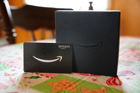 Amazon gift card and black gift box on a festive holiday tablecloth, representing e-commerce, retail branding, and Christmas shopping.