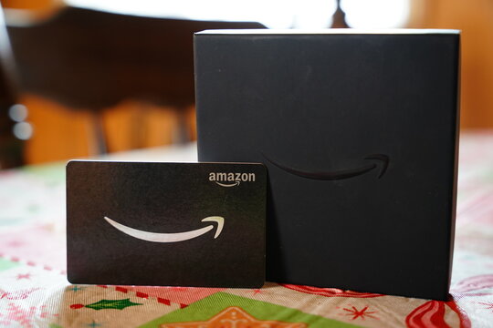 Amazon gift card and black gift box on a festive holiday tablecloth, representing e-commerce, retail branding, and Christmas shopping.