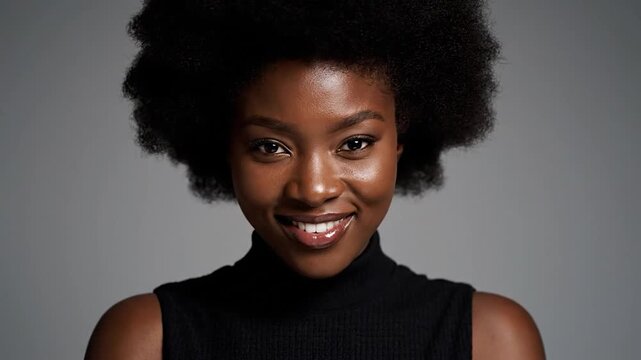 Portrait of a woman with black hair and a radiant smile, wearing black on a grey background