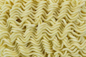 Close-up texture of dry instant noodles block, showing detailed wavy pattern and yellow monochromatic abstract background.