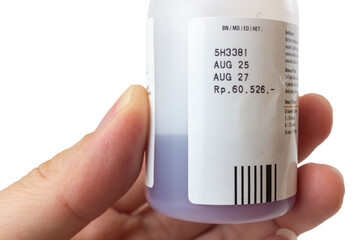 Male hand holding a white plastic medicine bottle with a purple liquid syrup inside. The label clearly shows the manufacturing and expiration dates (AUG 25 and AUG 27), isolated on a white background.