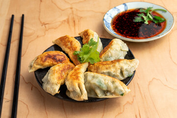 A plate of Dim Sum potsticker dumplings and soy dipping sauce with chopsticks on a plain wooden table