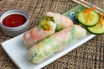 A white plate of Vietnamese rice paper shrimp fresh rolls with dipping sauce  with fancy chop sticks on a woven mat