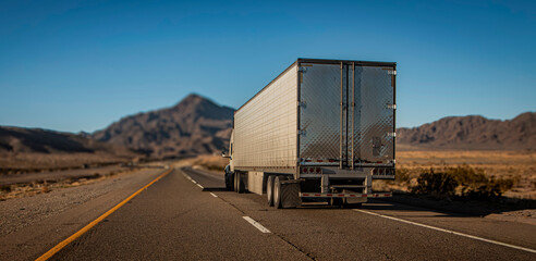 Following behind a white truck on a two lane highway in the desert with a rocky hill in the...