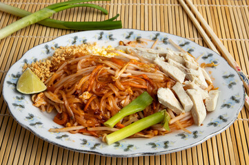 A fancy plate of chicken Pad Thai dinner with fancy chop sticks on a bamboo mat