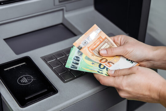 Individual withdrawing cash from an ATM, holding various euro banknotes, showcasing modern banking technology and the convenience of electronic transactions in everyday life