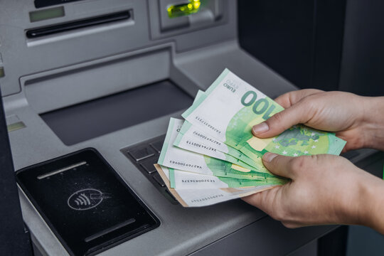 Hands holding cash banknotes of various denominations, withdrawing money from an ATM machine, showcasing the process of cash withdrawal and financial transactions