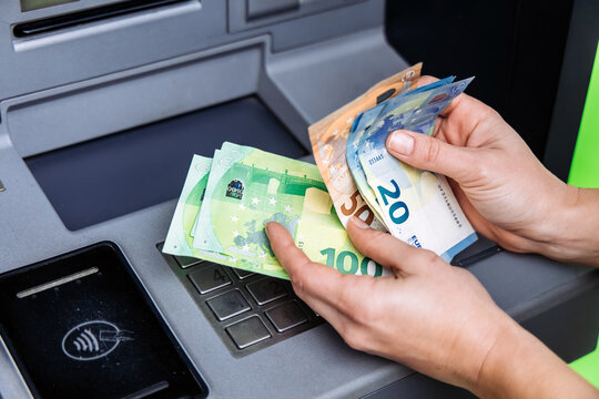 Hands of a person withdrawing cash from an ATM, showcasing various euro banknotes, with a focus on the transaction process and the machine's interface - Powered by Adobe