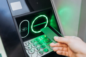 Hand holding a bank card near an ATM machine, with illuminated keypad and card reader, showcasing modern banking technology and user interaction in a financial setting
