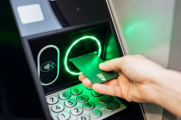 Hand inserting a contactless payment card into an ATM machine, illuminated keypad and screen displaying transaction options, showcasing modern banking technology and convenience