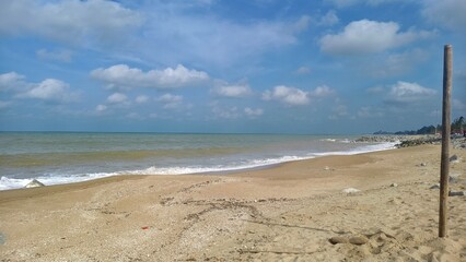 Coastal view featuring large grey rocks on a sandy shore with white waves crashing against the shoreline