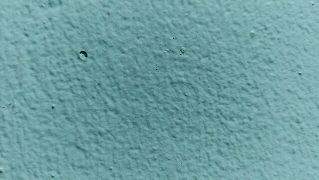 Detailed shot of a textured teal surface highlighting small craters, pockmarks, and irregular paint application patterns.
