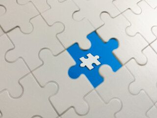 Fototapeta premium A white jigsaw puzzle with one missing piece revealing a vibrant blue background, featuring a tiny miniature piece at the center. Symbolizes problem-solving and innovation.