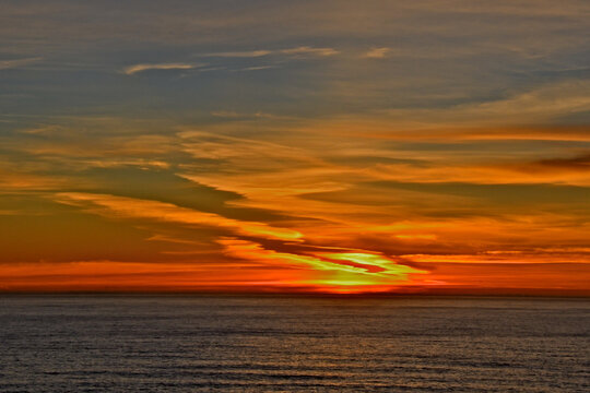 Fiery sunset as sun fall below horizon . Degrading contrails from jets coming in from Hawaii or Asia add diagonal interest 