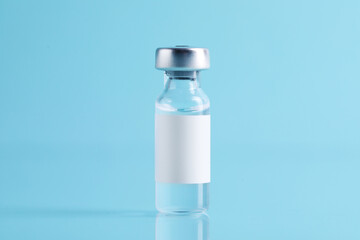 Vaccine in glass vial on mirror surface against turquoise background, closeup