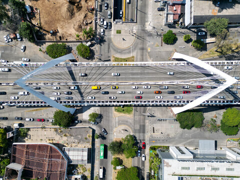 Aerial view of Matute Remus Bridge, Guadalajara. Modern cable-stayed bridge over busy traffic, city buildings and trees on a sunny day