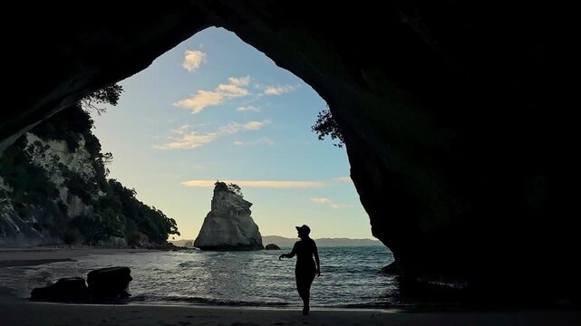 Silhouette of a woman walking out of Cathedral Cove cave in New Zealand