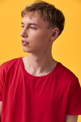 Fototapeta premium Young male in a red shirt against a bright yellow background, looking to the side, casual studio shot for fashion, lifestyle, color styling and contemporary mood.