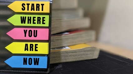 Colorful sticky notes with motivational message “Start Where You Are Now” beside books, symbolizing learning and personal growth.