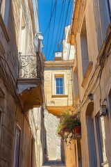 Sunlit narrow Mediterranean alley with warm stone facades, wrought iron balcony, window, cascading potted flowers and a peaceful nostalgic atmosphere