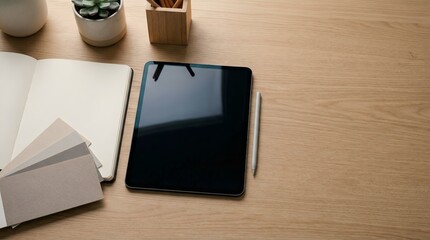 A tablet and notebook on a wooden desk with office supplies