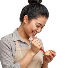 Focused young Asian woman decorating a heart-shaped cookie with red icing, expressing creativity on isolated transparent background.