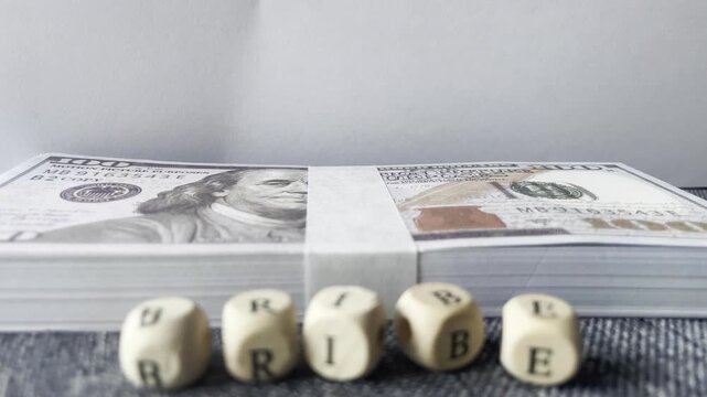 Close up view of wooden letter blocks spelling bribe in front of a blurred stack of cash