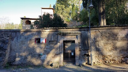 Rome, Italy &ndash; 14 January 2025. The gated entrance to the ancient Tomb of the Scipios sits embedded in a cracked stone wall on the Via Appia, surrounded by trees and shadows.
