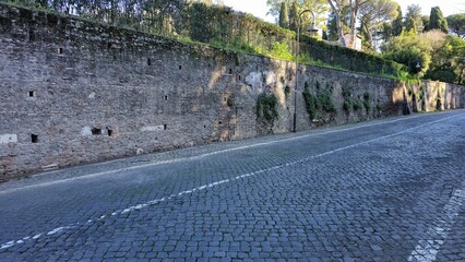 Rome, Italy &ndash; 14 January 2025. A quiet section of the Via Appia features cobblestones, tall stone walls with ivy, and lined lamp posts under morning light near the Tomb of the Scipios.