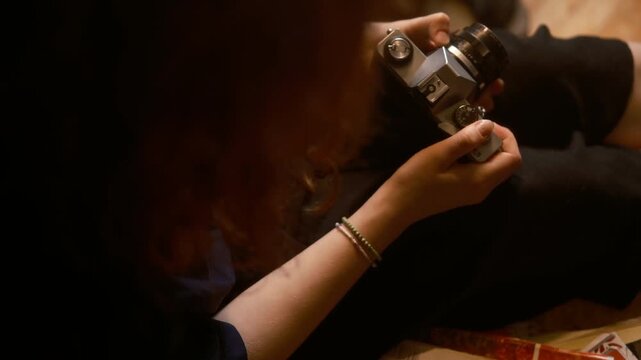 cinematic vintage top view close up, teenage girl with red hair holds a film camera at home. Intimate, nostalgic scene with analog photography warmth focus