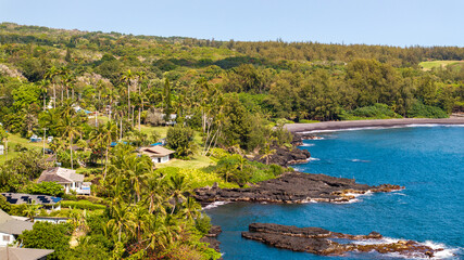 Fototapeta premium Aerial View of beachfront homes and surrounding lush green forest withblack sand beach in Hana coastal town of Maui, Hawaii landscape 