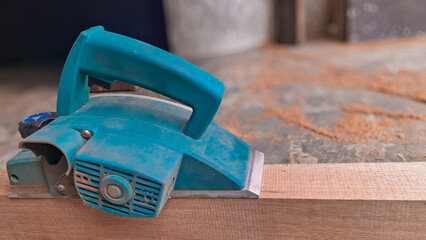 Teal electric wood planer resting on a timber plank in a carpentry workshop setting