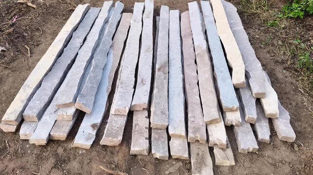 Rows of rectangular natural stone pillars laid on ground for agricultural fencing construction