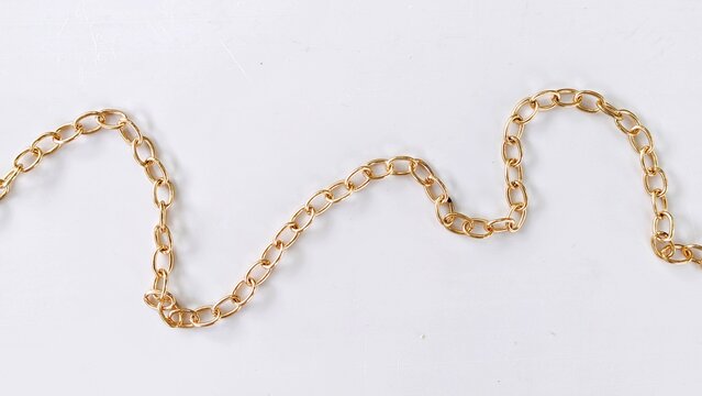 Wavy gold cable chain path laying flat on white background.