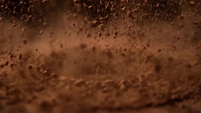 A small object falls into fine, reddish powder, creating concentric circles. Dark background