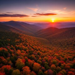 Aerial view of a mountain valley in autumn as the sun sets, casting an orange glow over rolling hills and colorful foliage