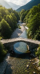 Aerial view of a stone bridge over a clear river, mountains in the distance and lush green trees along the banks