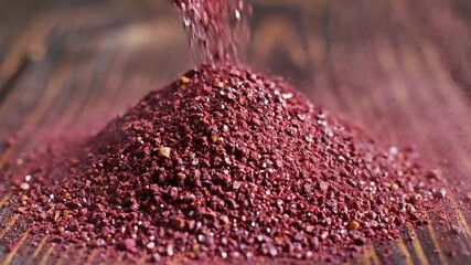 A vibrant cascade of small reddishmaroon granules possibly sumac or another exotic spice gracefully pours onto a rustic wooden surface forming an inviting and textured pile highlighting the natural b.