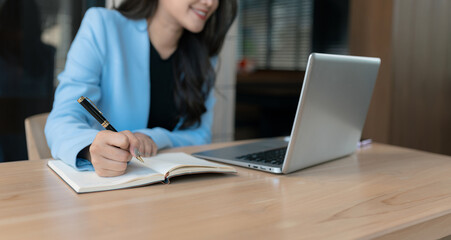 Business woman using computer working online, doing searching, taking notes looking at smartphone...