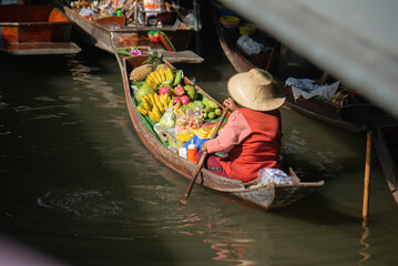 Obraz premium Local fruit vendor rowing a boat at a traditional Thai floating market.