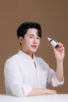 Portrait of a happy young Asian man prefect clean fresh skin holding a serum bottle.