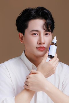 Portrait of a happy young Asian man prefect clean fresh skin holding a serum bottle.